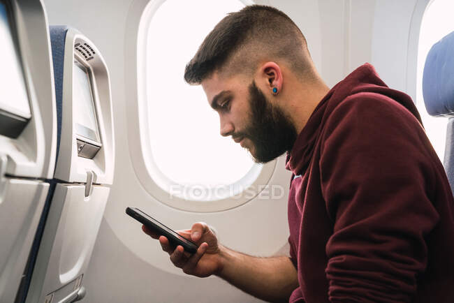 Barbudo cara usando smartphone no avião — Fotografia de Stock