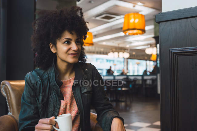 Mujer negra con cabello afro tomando un café en una cafetería - foto de stock