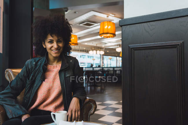 Femme noire aux cheveux afro buvant un café dans un café — Photo de stock