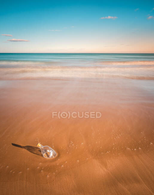 Bottiglia con lettera incastrata nella sabbia bagnata vicino al bellissimo mare ondulato — Foto stock