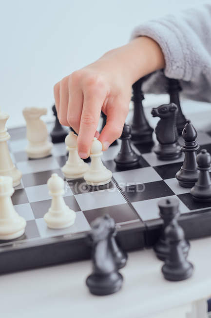 Cropped image of child holding figure on chess board on grey background — Stock Photo