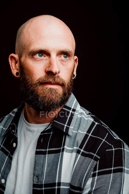 Бородатый хипстер в рубашке, смотрящий в камеру на черном фоне — стоковое фото