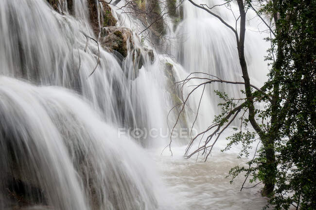 Increíble cascada alta que cae en el río cerca de la madera en Rio Cuervo, Cuenca, España - foto de stock