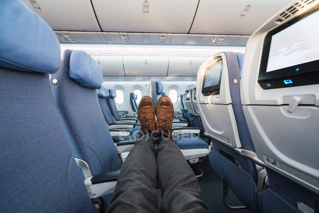 Ноги анонимного человека в стильных брюках и обуви лежат на удобных креслах внутри современного самолета — стоковое фото