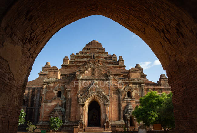 Bagan, Myanmar - 25 juin 2012 : vue majestueuse de l'ancien temple asiatique contre le ciel bleu à travers une arche minable — Photo de stock