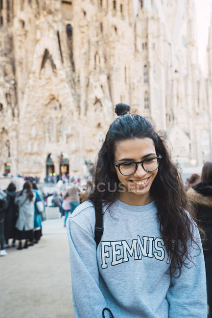 Preciosa joven en traje casual y gafas elegantes sonriendo mientras está parada en la calle en Barcelona, España - foto de stock