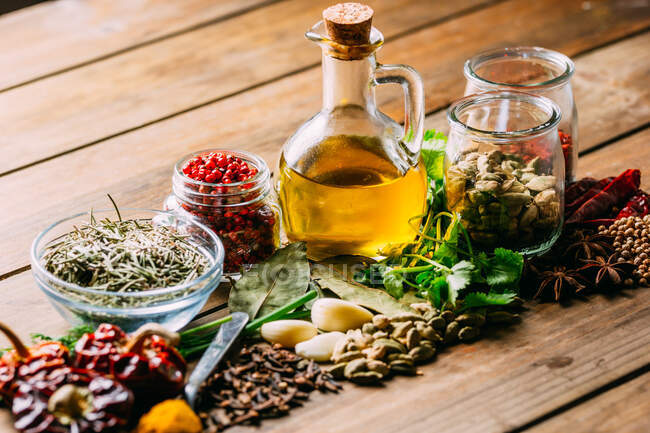 Разнообразные специи и травы и бутылка масла на деревянной столешнице — стоковое фото