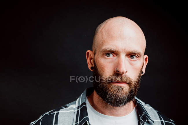 Bearded hairless hipster in shirt looking at camera on black background — Stock Photo