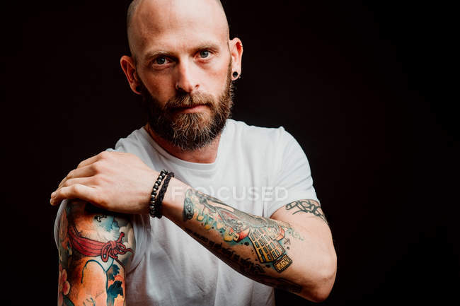 Hipster barbu sans poils en t-shirt montrant des tatouages sur les mains sur fond noir — Photo de stock