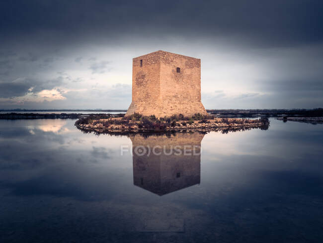 Magnífica vista de la antigua Torre del Tamarit reflejándose en la tranquila superficie del lago en un día nublado en Santa Pola, España - foto de stock
