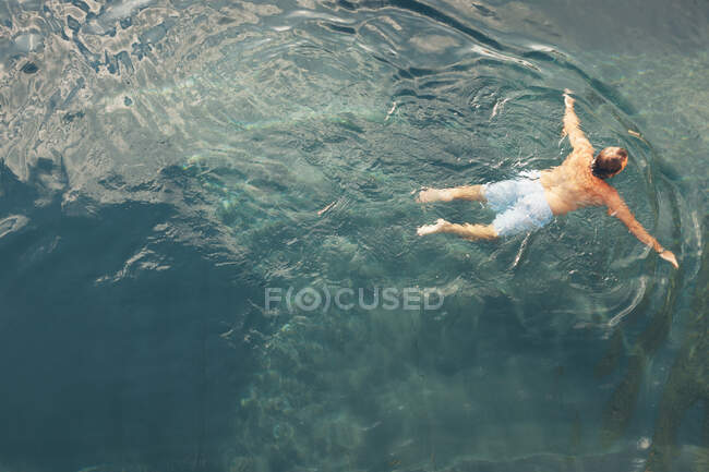 Desde arriba vista trasera del macho en pantalones cortos nadando en agua azul limpia - foto de stock