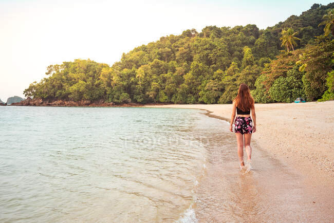 Rückansicht der schlanken Dame, die am Sandstrand in der Nähe des Meeres und des grünen tropischen Waldes in Jamaica spaziert — Stockfoto