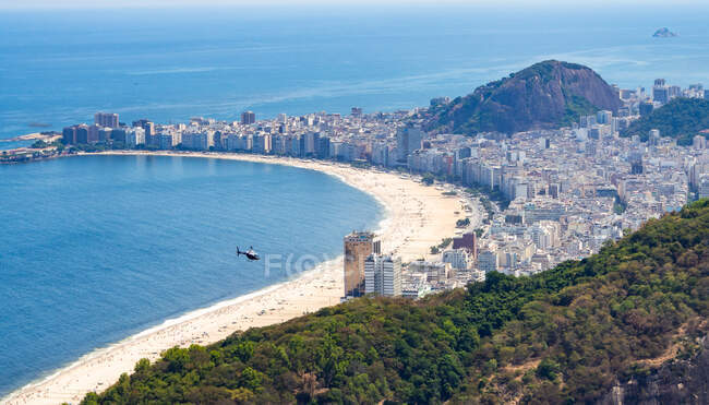 Majestic drone view of distant helicopter flying over sandy beach and modern coastal city in Brazil — Stock Photo
