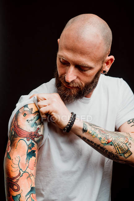 Hipster senza peli barbuti in t-shirt che mostra tatuaggi su mani su sfondo nero — Foto stock