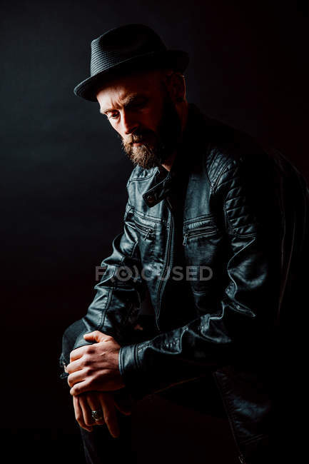 Холодный хипстер в шляпе и кожаной куртке смотрит в сторону на черном фоне — стоковое фото