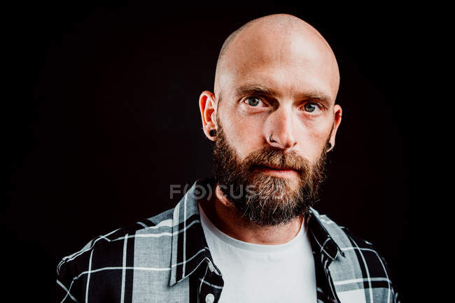 Bearded hairless hipster in shirt looking at camera on black background — Stock Photo