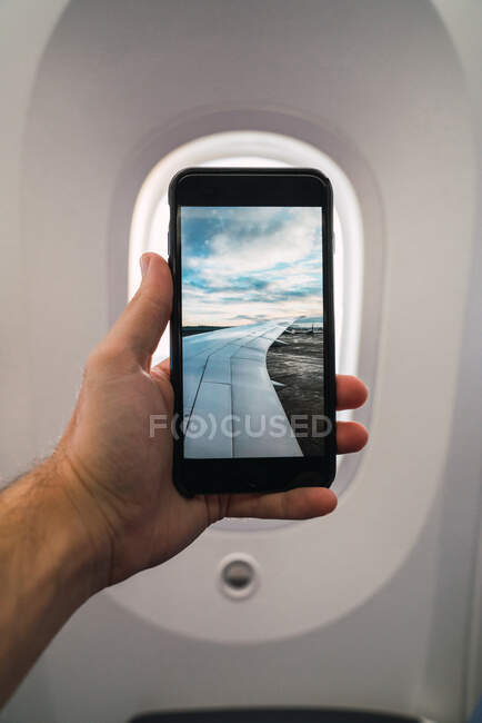Hand of anonymous male demonstrating smartphone with picture of airport inside modern aircraft — Stock Photo