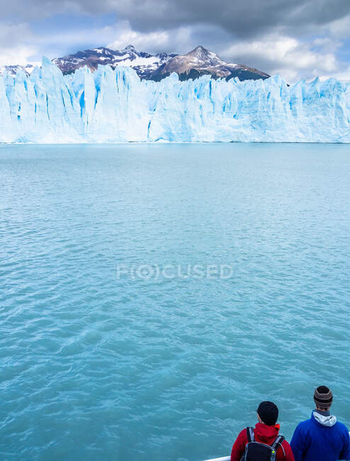 Back view of two tourists admiring calm cold sea and spectacular ice cliff on cloudy day in Argentina — Stock Photo