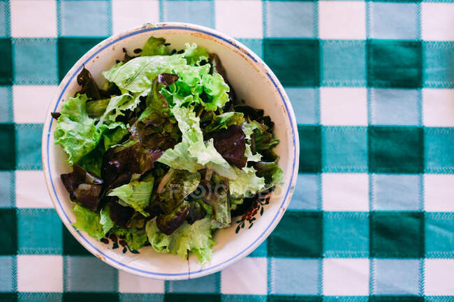 Von oben Schüssel mit gesundem Salat auf Tischplatte mit karierter Tischdecke — Stockfoto
