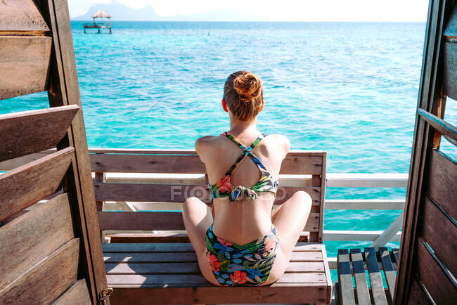 Visão traseira da senhora de maiô e óculos de sol sentados no assento perto do mar azul na Jamaica — Fotografia de Stock