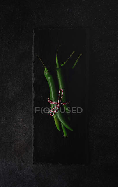 Fresh green spicy chilli peppers on slate on black background — Stock Photo