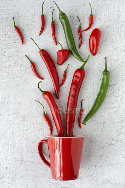 Fresh red and green spicy chilli peppers on white background with mug — Stock Photo