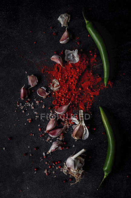 Fresh green chilli peppers, garlic cloves and spices on black background — Stock Photo