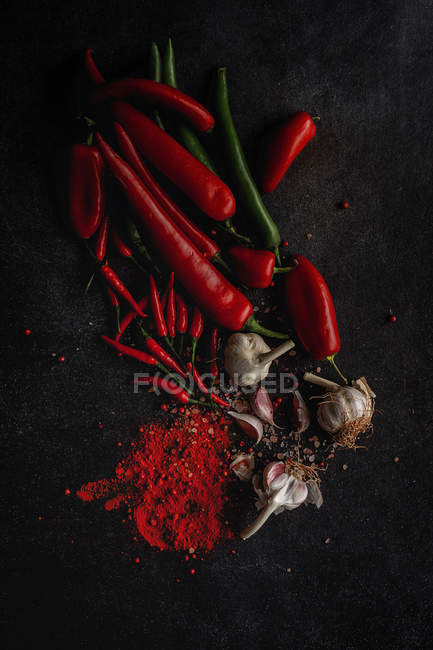 Fresh red and green chilli peppers, garlic cloves and spices on black background — Stock Photo