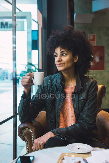 Черная женщина с афроволосами пьет кофе в кофейне — стоковое фото