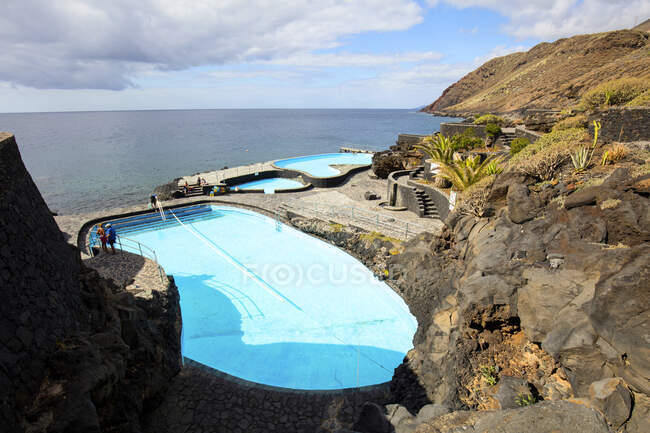 De piscinas acima na costa rochosa perto da superfície da água e céu nublado na Ilha Hierro, Ilha Canária, Espanha — Fotografia de Stock