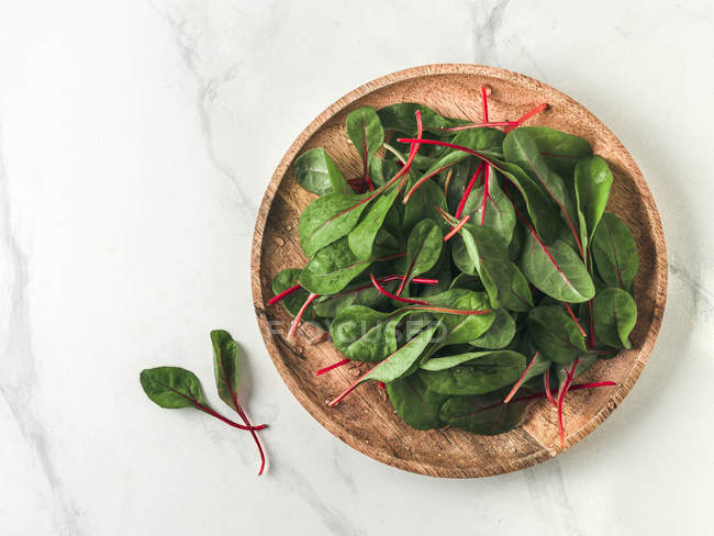 Fresh green chard leaves on wooden plate on white marble background — Stock Photo