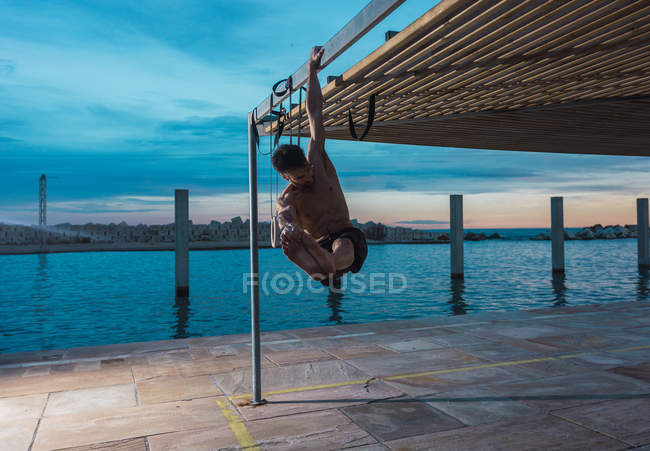 Homem atlético equilibrando em anéis de ginástica em aterro na cidade da noite — Fotografia de Stock