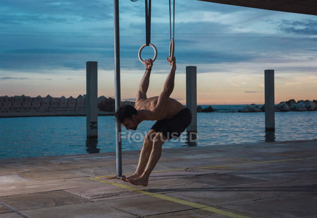 Спортсмен балансує на гімнастичних кільцях на набережній у вечірньому місті — стокове фото