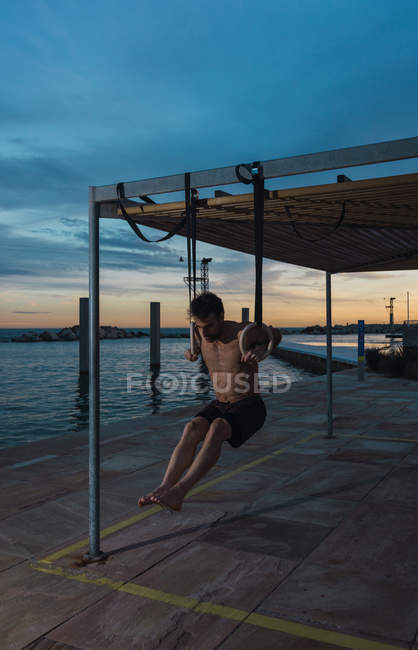 Homme athlétique équilibrage sur les anneaux de gymnastique sur le remblai dans la ville du soir — Photo de stock