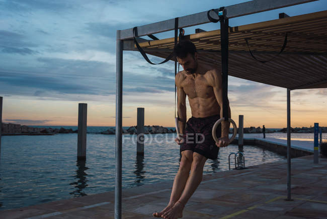 Sportlicher Mann balanciert auf Turnringen am Damm in der Abendstadt — Stockfoto