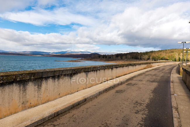 Landscape of perspective empty promenade with concrete fence under cloudy sky and with mountains on background — Stock Photo