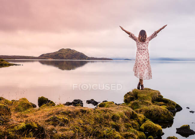 Rückansicht einer Reisenden, die am Seeufer steht und in Island die Hände hochzieht — Stockfoto