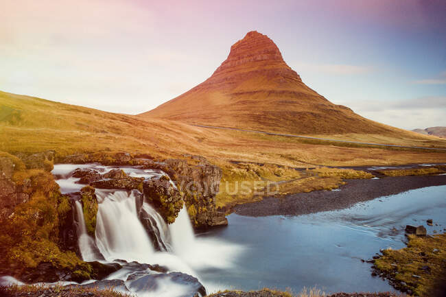 Landscape of beautiful waterfalls in long exposure on coast of river with green mountain peak on background, Iceland — Stock Photo