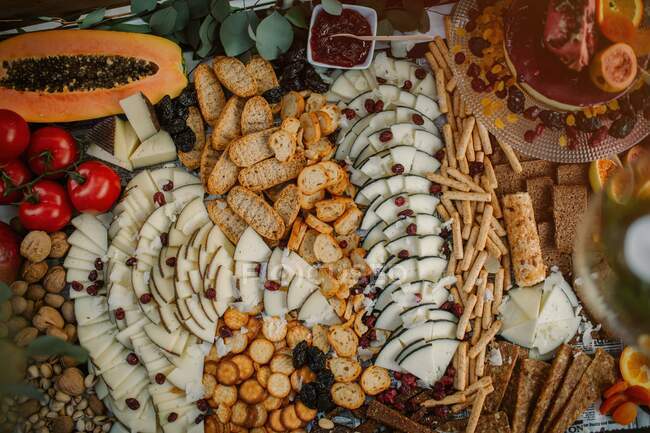 Зверху розташовані різноманітні закуски з крекерами, фруктами, горіхами та овочами на столах — стокове фото