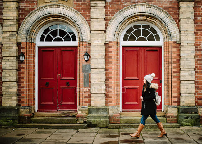 Vista lateral de la mujer turística caminando a las puertas rojas del edificio de ladrillo en la calle en York, Inglaterra - foto de stock