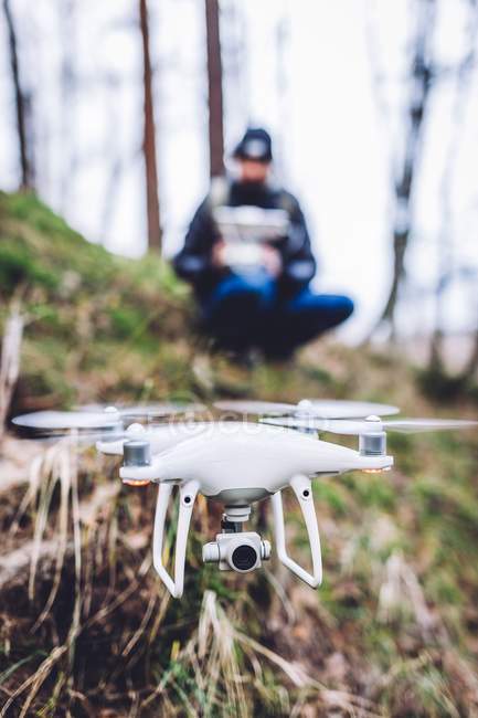 Gars avec télécommande opérant drone volant sur la colline entre les arbres sur fond flou — Photo de stock
