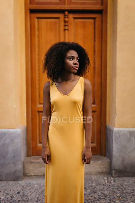 Elegant black woman in yellow dress standing on street and looking away — Stock Photo