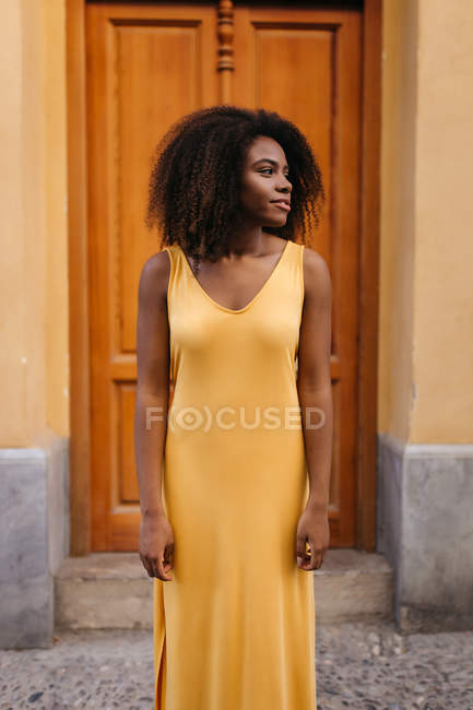 Mulher negra elegante em vestido amarelo em pé na rua e olhando para longe — Fotografia de Stock