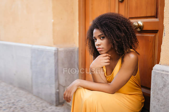 Magnifique femme noire en robe assise sur le porche sur la rue — Photo de stock