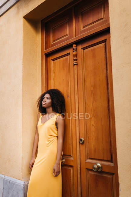 Pensive femme noire en robe jaune appuyé sur la porte sur la rue — Photo de stock