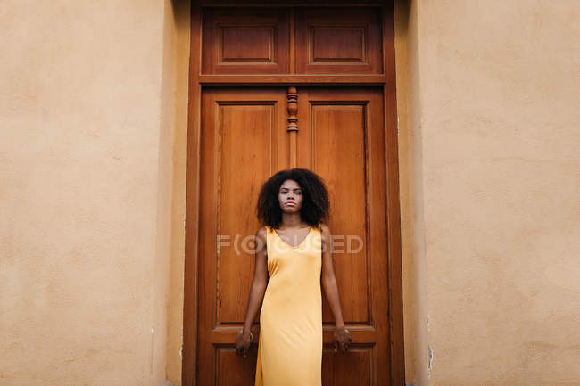 Hinreißende schwarze Frau im Kleid posiert vor Holztür auf der Straße — Stockfoto