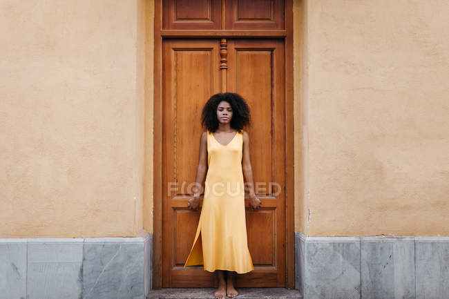 Sonhador mulher negra em vestido amarelo inclinando-se na porta na rua — Fotografia de Stock