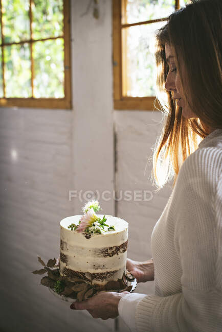 Donna sorridente in possesso di piatto con torta decorata da fiori e p — Foto stock
