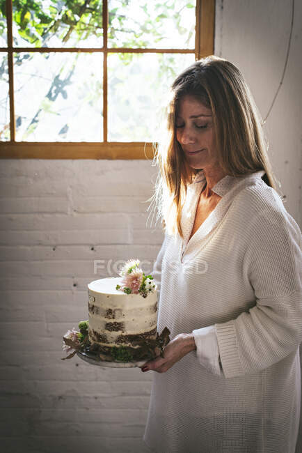 Smiling woman holding plate with cake decorated by flowers and p — Stock Photo