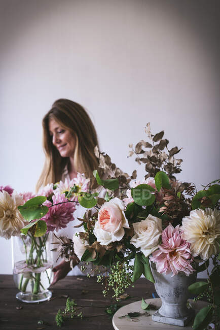 Donna vicino al tavolo con mazzi di fiori in vasi — Foto stock
